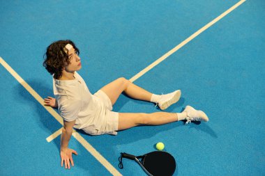 Spor kıyafetleri içinde dinamik bir genç adam Padel oynadıktan sonra dinleniyor, çevikliğini ve dikkatini gösteriyor..