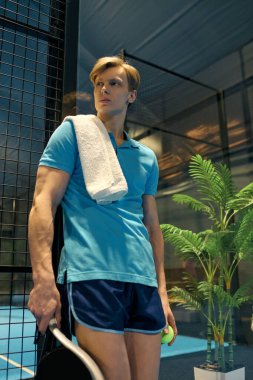 Atletik genç adam padel kortunda dinleniyor, omuzlarında havlu, oynamaya hazır..