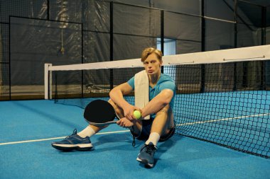 Mavi kortta Padel oynadıktan sonra ağları eşeleyen genç bir atlet.