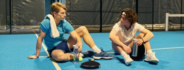 İki genç Padel oyuncusu taktikleri paylaşıyor ve sahadaki rekabetçi bir maçtan sonra rahatlıyorlar..