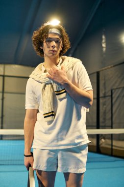 Genç bir adam şık bir kortta Padel oynarken atletik hünerini gösteriyor..