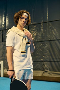 Spor kıyafetleri giymiş genç bir atlet canlı bir kortta Padel oynamaya hazırlanıyor..