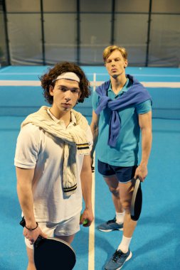 İki genç adam parlak bir padel kortunda kürek çekiyor, odaklanmış ve harekete hazır..