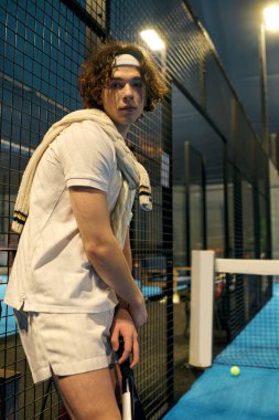 Atletik giyimli genç bir adam Padel oynamaya hazırlanıyor. Konsantrasyon ve atletizm gösteriyor..