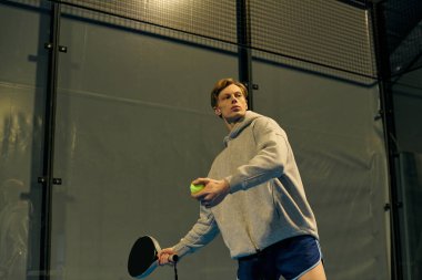 Genç bir adam Padel sahasında atletizm sergileyen güçlü bir atış için ustalıkla hazırlanıyor..