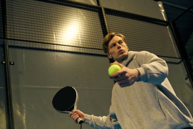 Spor kıyafetleri giymiş genç bir adam Padel Balosu 'na odaklanıp kararlılıkla hizmet etmeye hazırlanıyor..