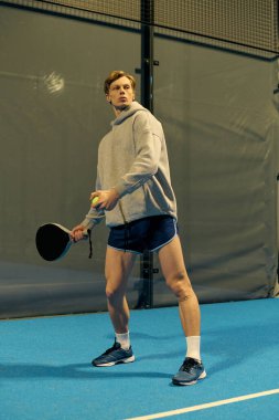 Genç sporcu Padel kortunda topa vurmaya hazırlanırken dikkatle odaklanıyor..