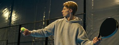 Genç bir adam Padel kortunda topa vurmaya hazırlanıyor, atletizm ve odaklanmayı gösteriyor, afiş.