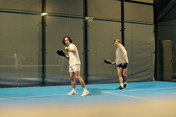 Два молодых спортсмена участвуют в соревновательной игре во время захватывающего матча в помещении.