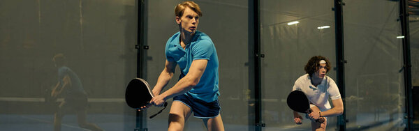 Два молодых человека демонстрируют свои навыки во время игры в падель, сосредоточены и конкурентоспособны на практике, баннер