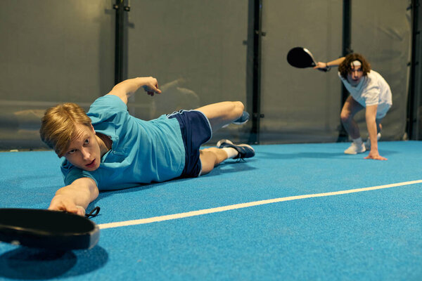 Two young men engage in an intense match of padel, demonstrating athleticism and focus.