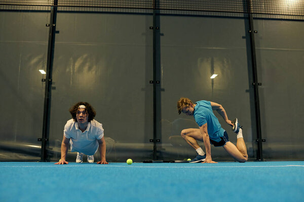 Два молодых спортсмена демонстрируют свои навыки перед тем, как играть в падель в современном зале суда.