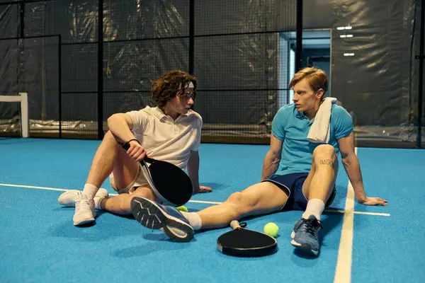 İki genç sporcu Padel kortunda gevşeyip, enerjik bir oyun sonrası sohbet ediyorlar..