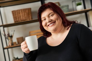 Zarif kadın, sanatsal çalışma alanında yaratıcılığa dalmışken elinde bir bardak tutuyor..