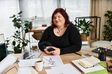 Kendine güvenen bir kadın, çizimler, bitkiler ve yaratıcı aletlerle çevrili huzurlu bir sanat stüdyosunda oturuyor..