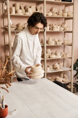 Yakışıklı adam sanatsal yaratıklarla çevriliyken kilden bir kap oluşturmaya odaklanıyor..