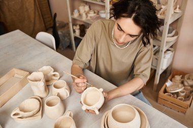 Şık bir adam yaratıcı çalışma alanında kil çömlek yontuyor, sanatını sergiliyor..