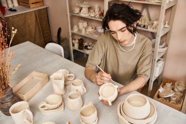 Yakışıklı adam, canlı bir çömlek atölyesinde el yapımı seramik bir parçayı dikkatlice dekore ediyor..