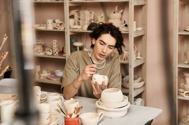 Yakışıklı ve şık bir adam, sanat eserleriyle çevrili canlı bir seramik stüdyosunda çömlek boyuyor..