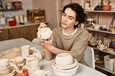 Yakışıklı bir adam sanatsal eserlerin ortasındaki yeni bir çömlek parçasına karmaşık tasarımlar çizer..