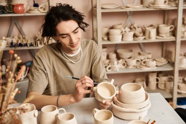 Yaratıcı genç adam sanatla dolu canlı bir çömlek atölyesinde titizlikle killeri şekillendiriyor..