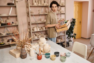Sanatsal malzemeler ve el yapımı seramiklerle çevrili yaratıcı bir adam çömlekçilikle uğraşır..
