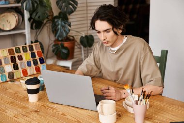 Şık bir adam stüdyosunda yaratıcı malzemelerle çevriliyken çömlek tasarımlarına odaklanmış..