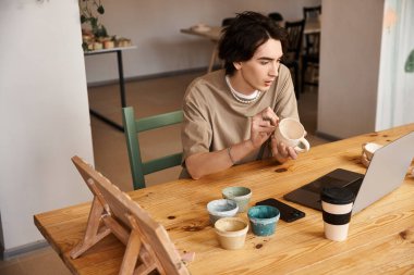 Çamura batmış yakışıklı bir adam, stüdyoda renkli seramiklerle çevriliyken killeri şekillendiriyor..