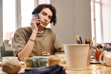 Yakışıklı adam stüdyoda renkli çömlek malzemeleriyle çevriliyken telefonla bağlantı kuruyor..