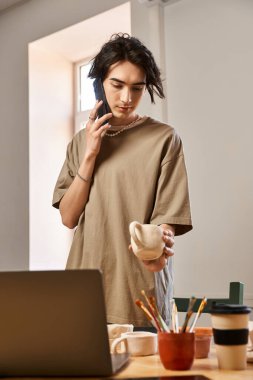 Bir adam stüdyosundaki telefon görüşmelerini yönetirken yaratıcı bir şekilde çömlekçilik yapıyor..