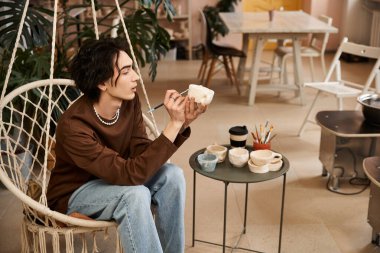 Sanat malzemeleri ile çevrili rahat bir stüdyoda otururken yaratıcı bir adam çömlek şekillendirir..