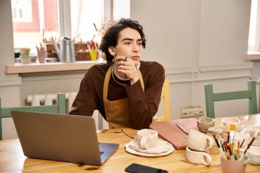 Önlüklü düşünceli bir adam bir sonraki seramik çalışmasını parlak bir stüdyoda yapmayı düşünüyor..