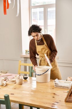 Yakışıklı bir adam, parlak ve ilham verici bir çömlek atölyesinde kil topuna kişisel dokunuşunu ekler..