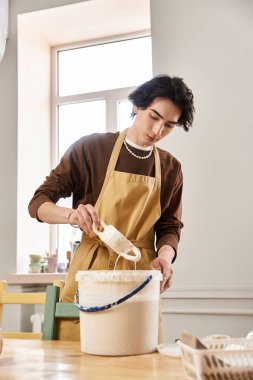 Yakışıklı bir adam, yaratıcı aletlerle çevrili, parlak bir stüdyoda çömlek yapmaya odaklanmış..