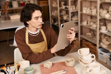 Çömlekçilikle uğraşan şık bir adam, sanatsal bir ortamda dijital aletlerden ilham alıyor..
