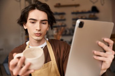 Çömlek atölyesindeki adam elinde bir kap tutuyor ve bir tablete odaklanıyor. Geleneği teknoloji ile birleştiriyor..