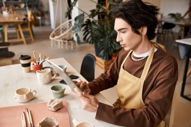 Yakışıklı adam sanatsal aletler ve dekorla çevrili yaratıcı çömlekçilik projeleriyle uğraşıyor..