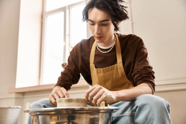 Bir çömlek atölyesindeki yakışıklı bir adam, yaratıcılığa dalmış, tekerleğin üzerindeki çamuru tutkuyla şekillendirir..
