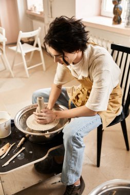 Yakışıklı ve şık bir adam, sanatla dolu parlak bir çömlek atölyesinde, tekerlek üzerinde kil şekillendirir..