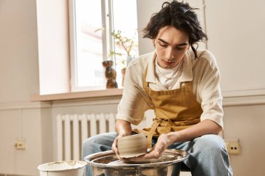 Yakışıklı adam yaratıcı bir stüdyo ortamında çömlek çarkında kil kalıplarını ustalıkla şekillendiriyor..