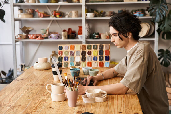 Творческий человек за деревянным столом фокусируется на керамике среди красочной керамики в студии.