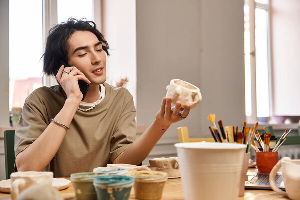 Стильный человек, занимающийся керамикой, разговаривающий по телефону, изучая свою работу.