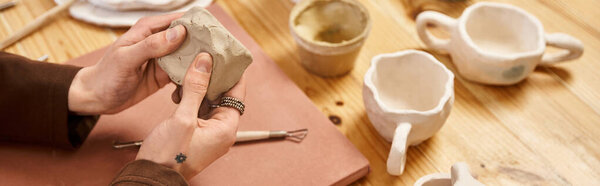 Красивый стильный мужчина искусно литет глину в керамической студии в окружении готовых работ.