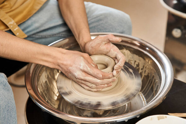A stylish man skillfully shapes clay on a pottery wheel in a vibrant artist studio.