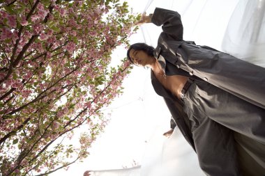 Tarz sahibi genç adam, çiçek açan kiraz çiçekleri arasında güvenle poz verirken doğanın tadını çıkarıyor. Polietilen, sürdürülebilirlik kavramı.