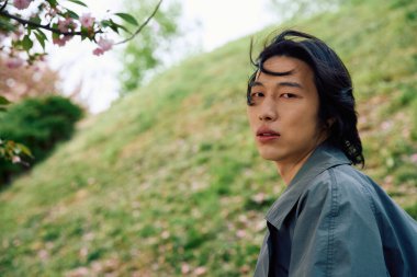 Huzurlu bir parkta, gri elbiseli genç bir Asyalı rahatlarken kendine güvenini ifade eder..