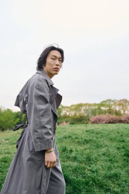 Genç bir Asyalı huzur parkında geziyor, şık gri bir kıyafet sergiliyor..