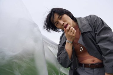 Genç bir Asyalı, polietilen yakınlarında şık gri bir elbise içinde poz veriyor.