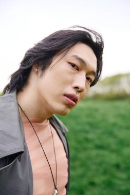 Parkta güneşli bir günün keyfini çıkarırken gri bir trençkot giyen şık, genç bir Asyalı..