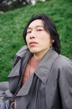 Genç bir Asyalı, doğanın tadını çıkarırken şık bir gri elbiseyi sergileyerek parkta uzanır..